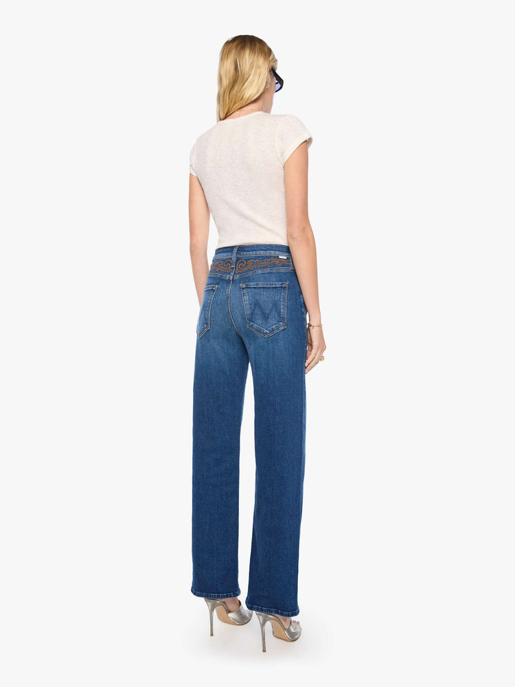 Back view of a woman in a med blue jeans designed to sit on the hips with a zip fly, slouchy fit, loose straight leg and a 32-inch inseam with a clean hem.