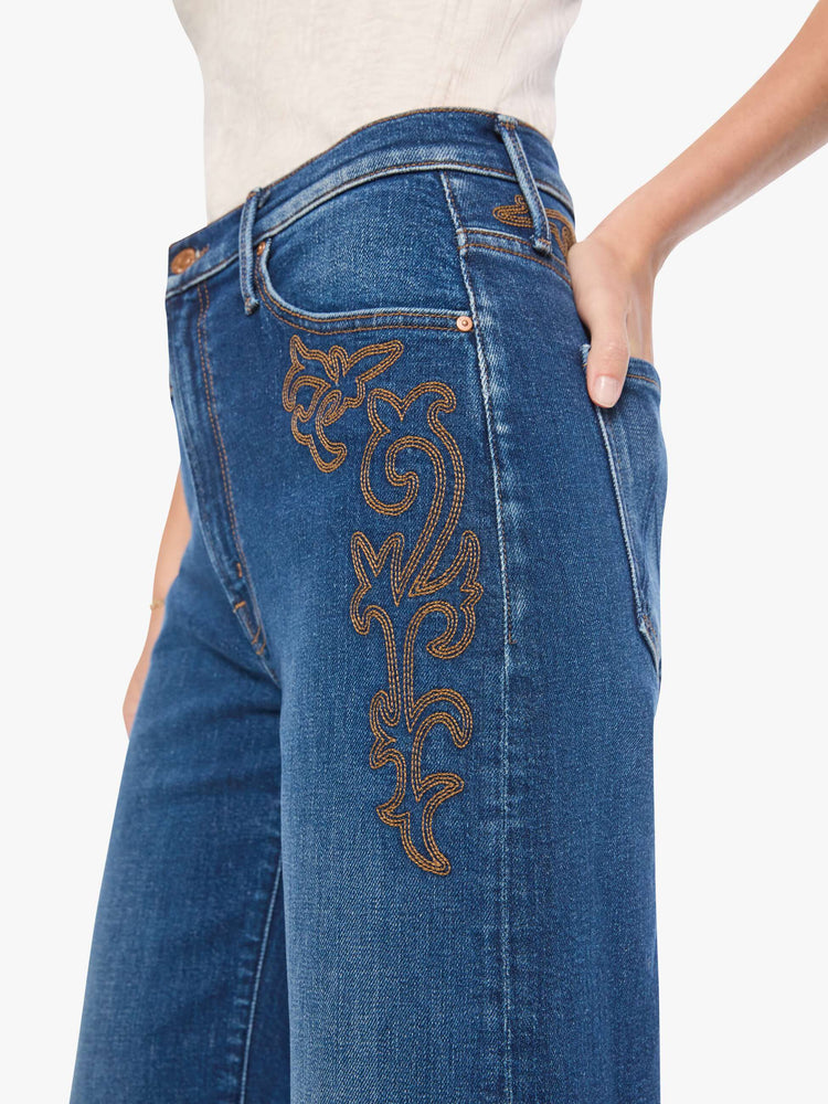 Close up view of a woman in a med blue jeans designed to sit on the hips with a zip fly, slouchy fit, loose straight leg and a 32-inch inseam with a clean hem.