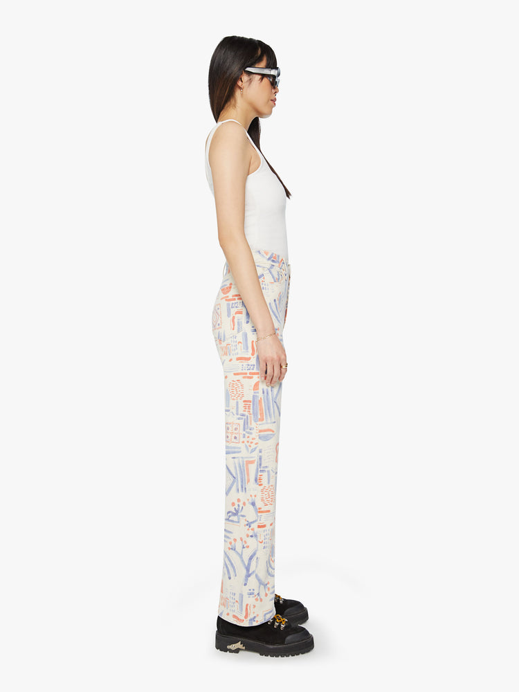 Side view of a woman super high-waisted pants with a loose fit, wide leg and 31-inch inseam with a clean hem in an off white with doodles in red and blue.