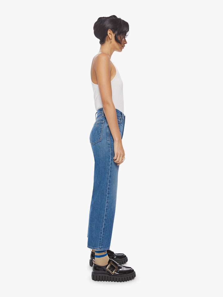 Side view of a woman high waisted jean with a wide straight leg, zip fly and clean ankle-length inseam in a med blue wash with studded text on the back.