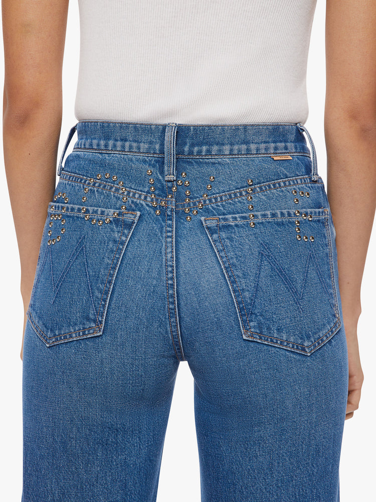 Close up back view of a woman high waisted jean with a wide straight leg, zip fly and clean ankle-length inseam in a med blue wash with studded text on the back.