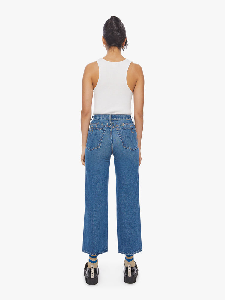 Back view of a woman high waisted jean with a wide straight leg, zip fly and clean ankle-length inseam in a med blue wash with studded text on the back.