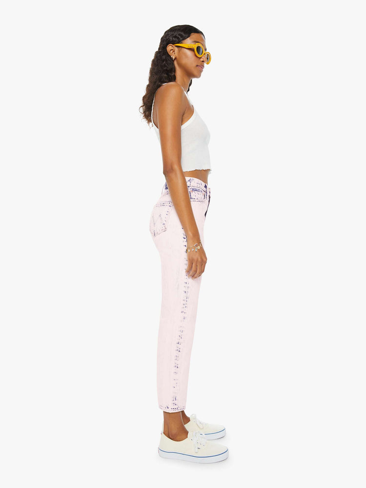 side view of a woman in ankle length jeans that are acid-washed and overdyed in a soft light pink with darker spots throughout.