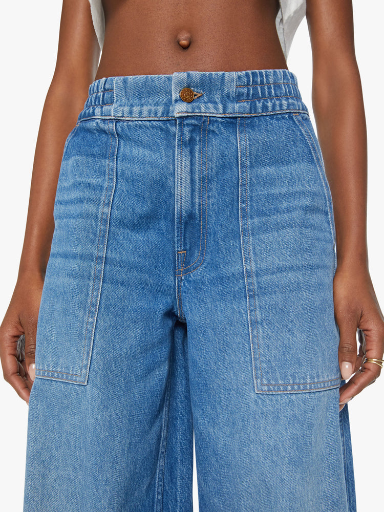 Close up view of a women ultra wide-leg jeans are designed with a high rise, elastic waist, drop crotch, utility-inspired patch pockets and a long 32-inch inseam with a cuffed hem in a mid-blue wash.
