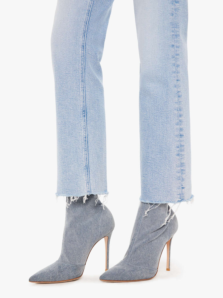 Front close up view of a woman wearing a light blue wash jean featuring an ankle length flare with frayed hem.