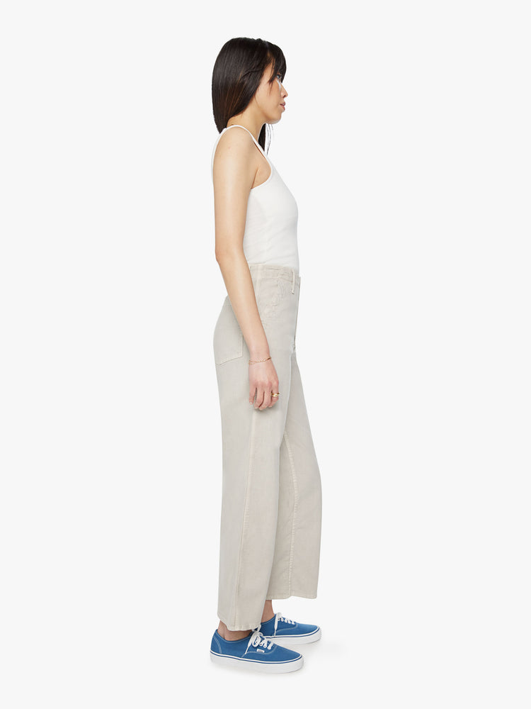 Side view of woman super high-waisted pants with a loose straight leg, zip fly, side slit pockets and an ankle-length inseam in an off white color.