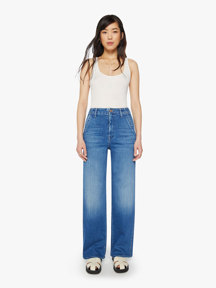 Front view of a woman mid-blue wash super high-rise straight-leg jean with a zip fly, wide leg, side slit pockets with braided details and a clean 31-inch inseam.