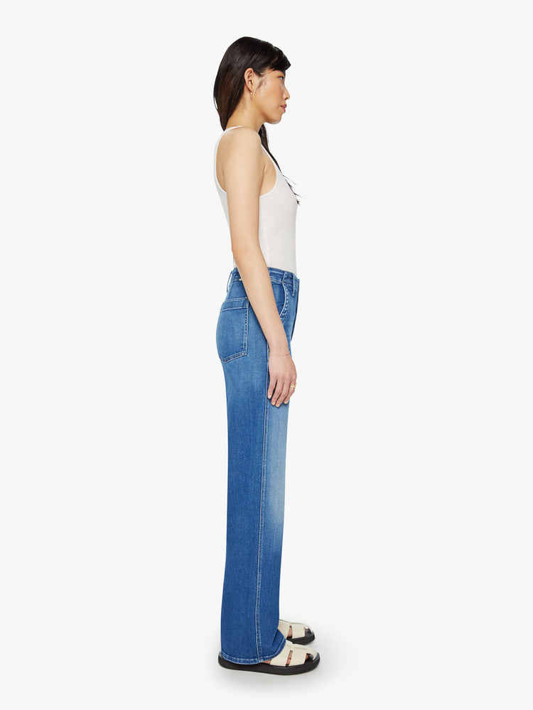 Side view of a woman mid-blue wash super high-rise straight-leg jean with a zip fly, wide leg, side slit pockets with braided details and a clean 31-inch inseam.