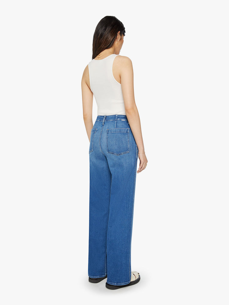 Back view of a woman mid-blue wash super high-rise straight-leg jean with a zip fly, wide leg, side slit pockets with braided details and a clean 31-inch inseam.