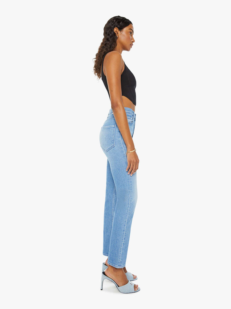 Side view of a woman in a light blue high-waisted straight leg jean with an ankle-length inseam, exposed button-fly and a clean hem.