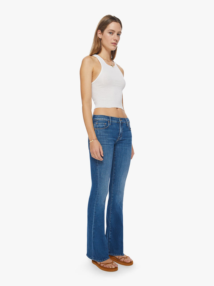 Side angle view of a woman super low-rise flares have a long 34-inch inseam and a clean hem in a mid- blue wash.