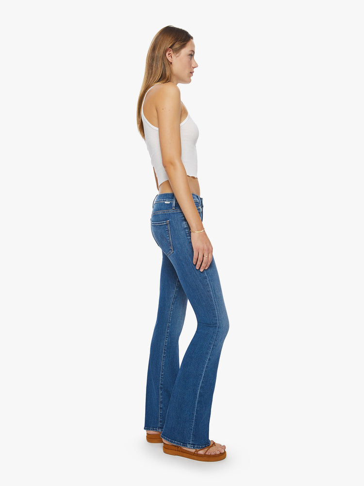 Side view of a woman super low-rise flares have a long 34-inch inseam and a clean hem in a mid- blue wash.