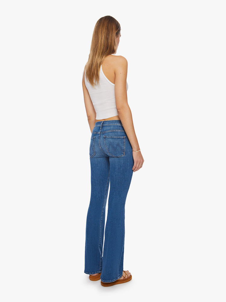 Back view of a woman super low-rise flares have a long 34-inch inseam and a clean hem in a mid- blue wash.