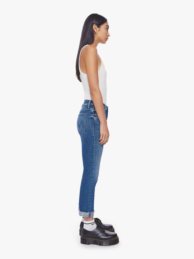 Side view of a woman button-fly jeans with a high rise and an ankle-length hem that's cuffed and frayed in a classic blue hue.