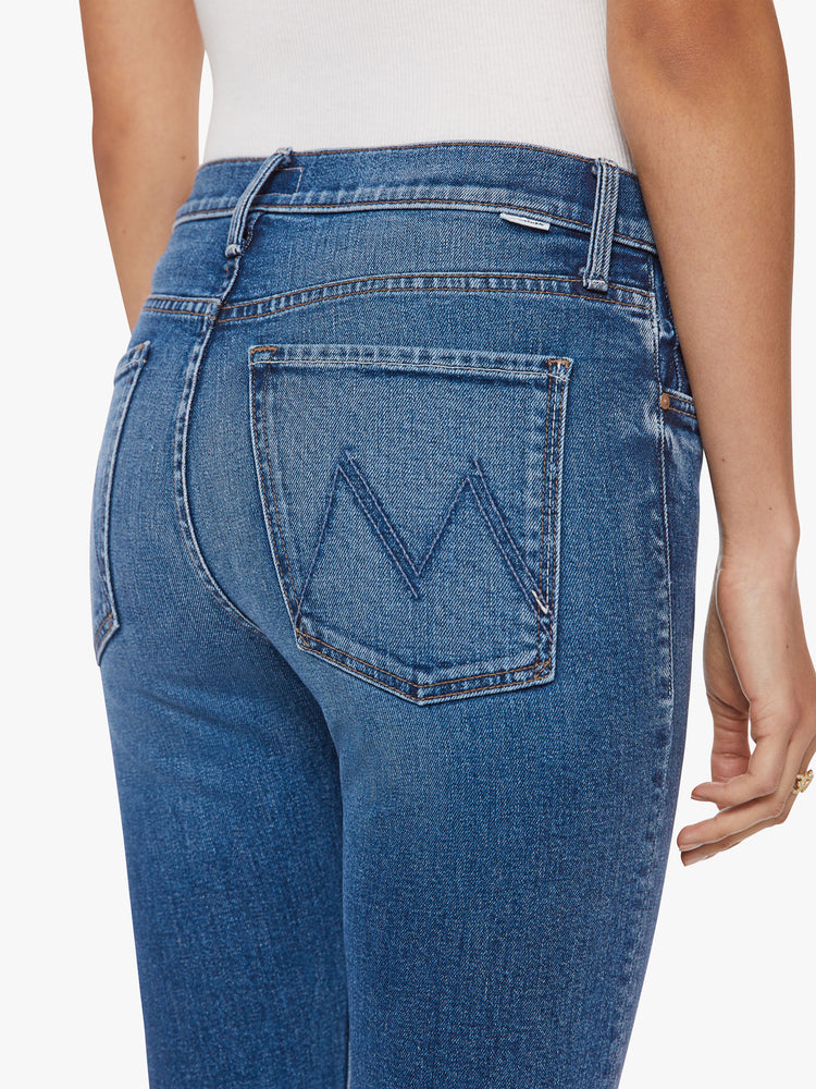 Close up back view of a woman button-fly jeans with a high rise and an ankle-length hem that's cuffed and frayed in a classic blue hue.