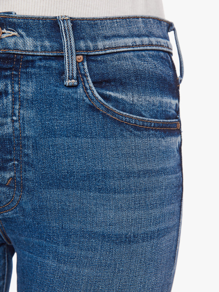 Front close up view of a woman button-fly jeans with a high rise and an ankle-length hem that's cuffed and frayed in a classic blue hue.