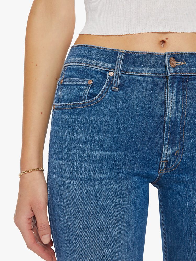 Close up waist view of a woman mid-rise straight-leg jeans with an ankle-length inseam and a clean hem in a mid-blue wash.