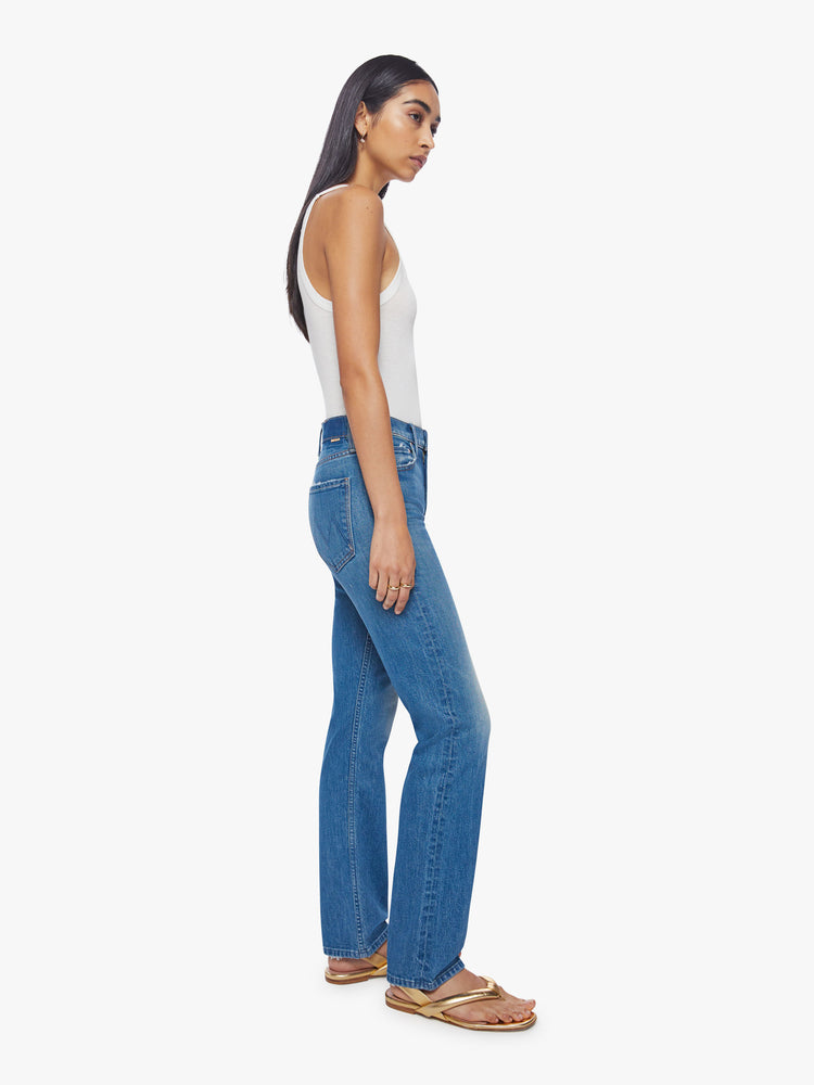 Side view of a woman high-rise jeans with a narrow straight leg and a 31-inch inseam with a clean hem in a mid-blue wash.