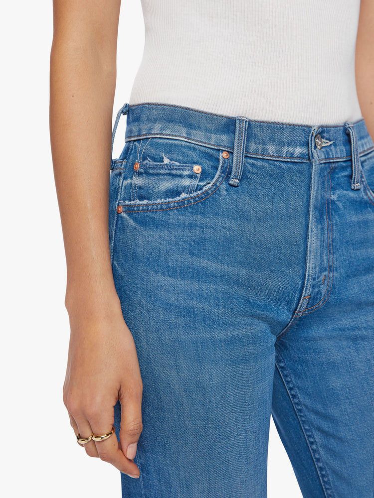 Close up waist view of a woman high-rise jeans with a narrow straight leg and a 31-inch inseam with a clean hem in a mid-blue wash.