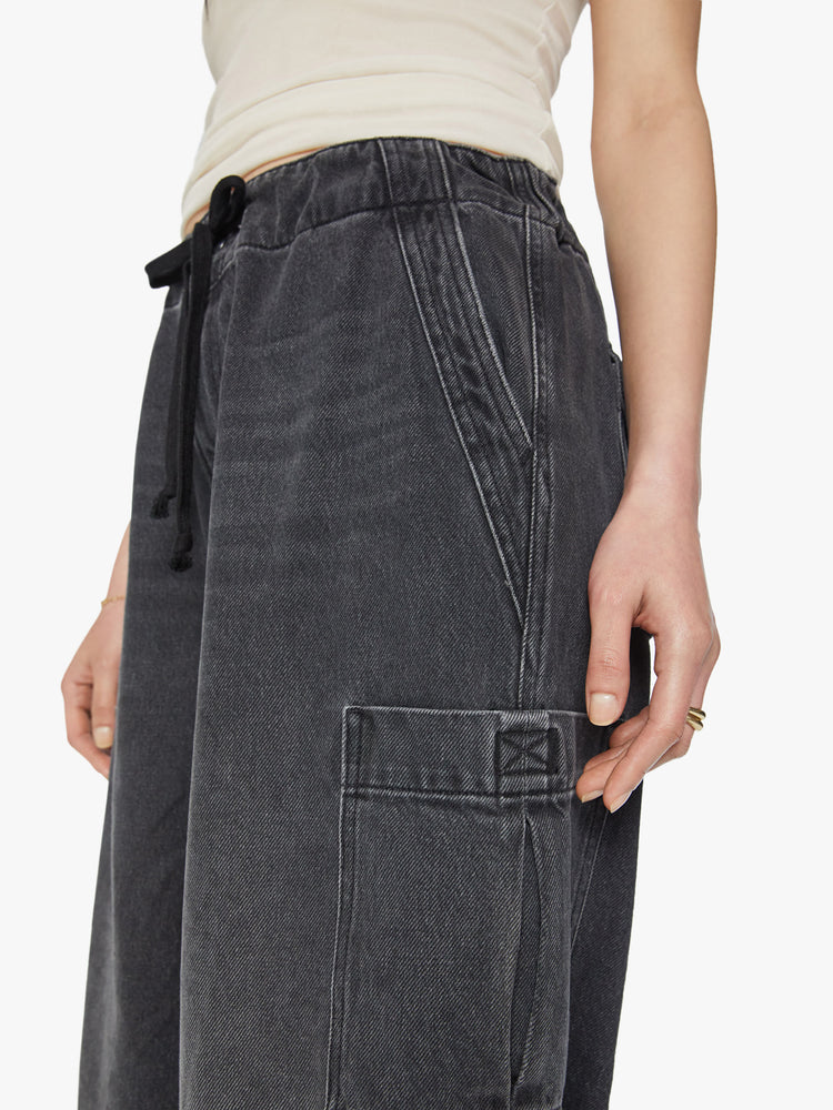 Waist close up view of a woman super high-waisted wide-leg jeans feature a drawstring waist, oversized utility pockets and an ankle-length inseam with an elastic drawstring at the hem in a faded black wash.