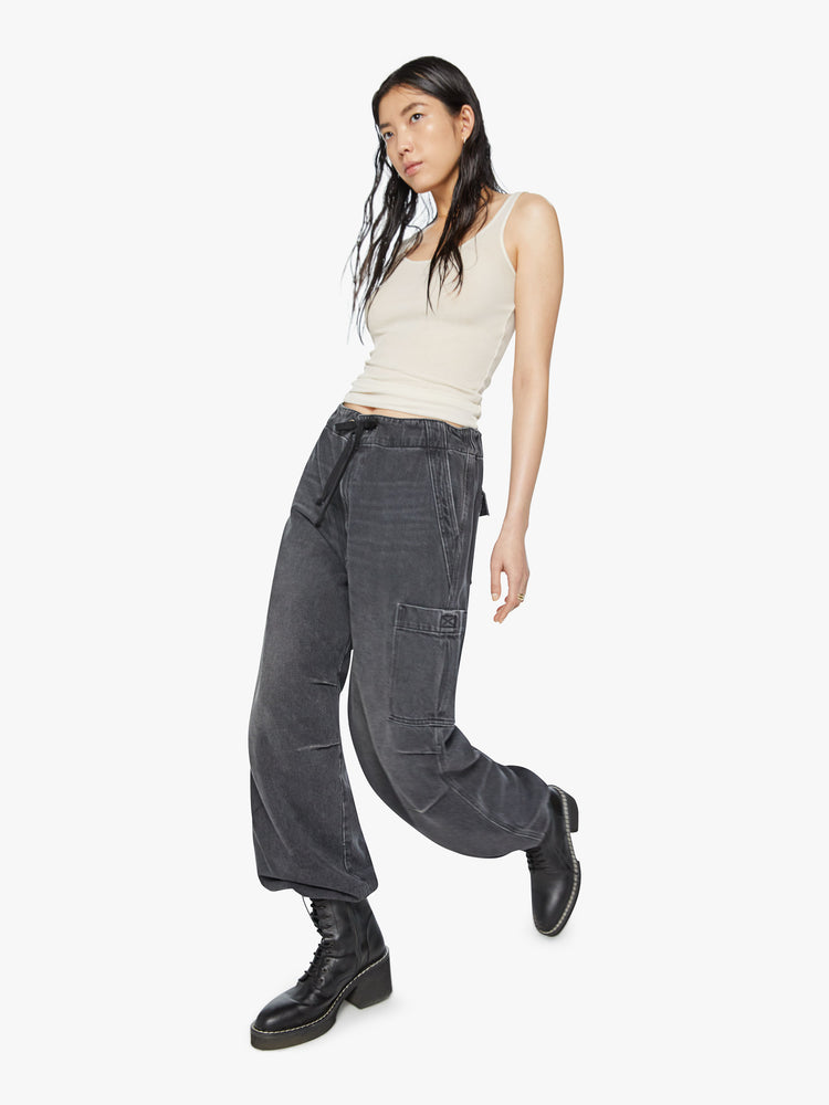 Walking view of a woman super high-waisted wide-leg jeans feature a drawstring waist, oversized utility pockets and an ankle-length inseam with an elastic drawstring at the hem in a faded black wash.