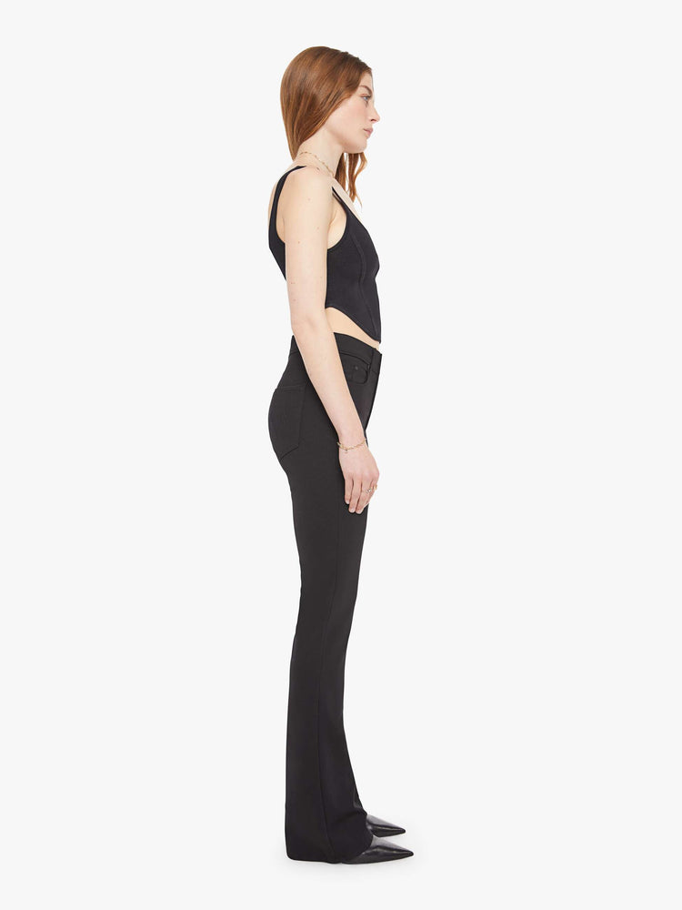 Side view of a woman in a black high-rise flared trouser with a zip fly and a 34-inch inseam with a clean hem.