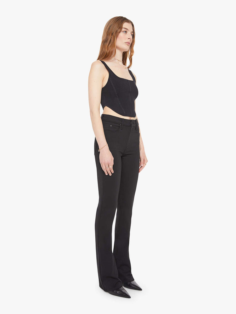 Front view of a woman in a black high-rise flared trouser with a zip fly and a 34-inch inseam with a clean hem.