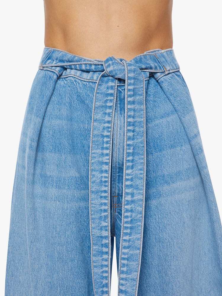 Close up view of a woman wide leg jean with super high-rise jeans feature a loose, full leg, a wrapped waist that ties in the front and a long 32-inch inseam in a mid blue wash.