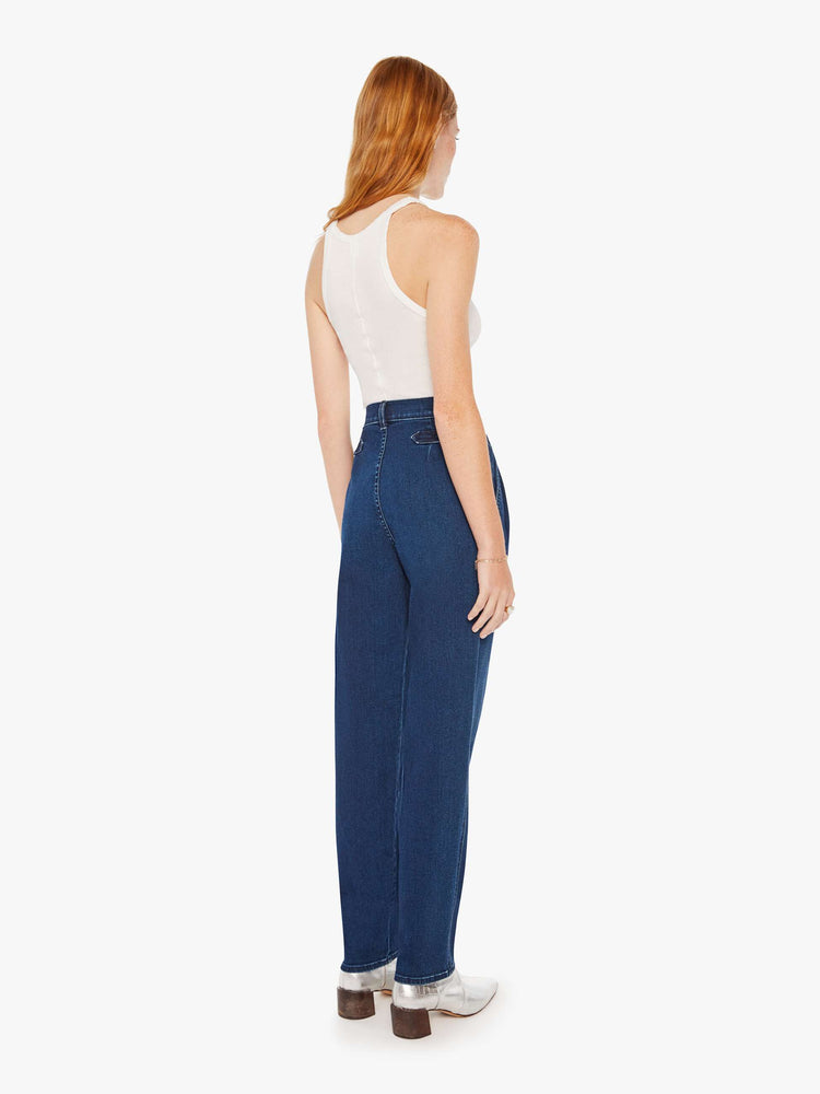Back view of a woman super high-rise jeans with pleated, adjustable tabs below the waist, side slit pockets, a long 31-inch inseam and a tapered straight leg in a dark blue wash.