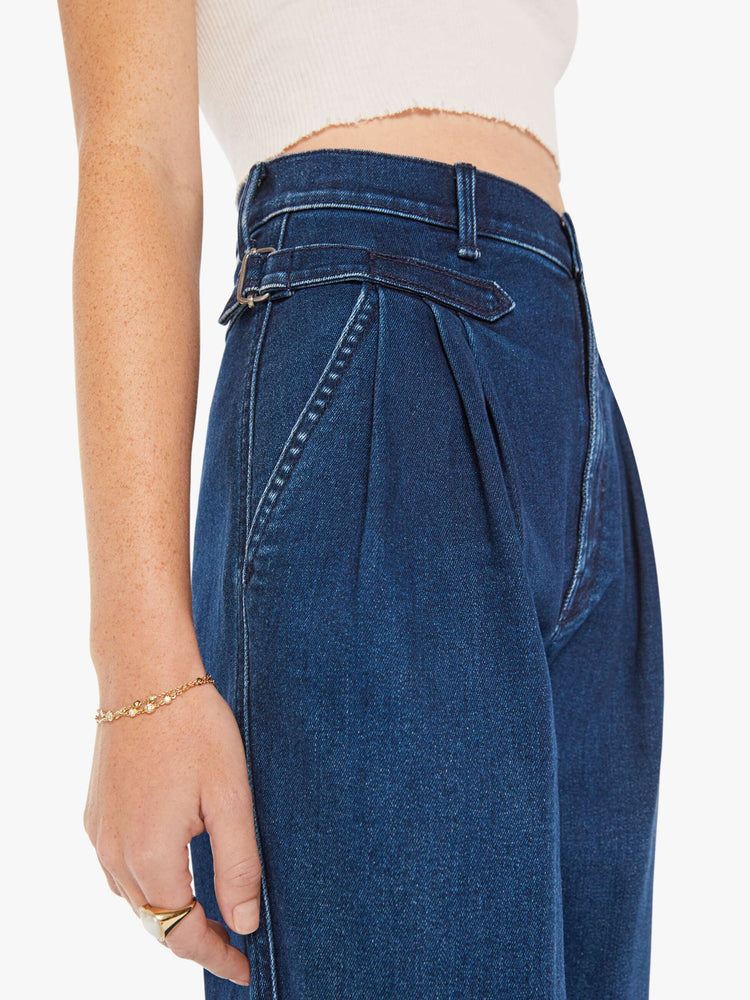 Waist close up view of a woman super high-rise jeans with pleated, adjustable tabs below the waist, side slit pockets, a long 31-inch inseam and a tapered straight leg in a dark blue wash.
