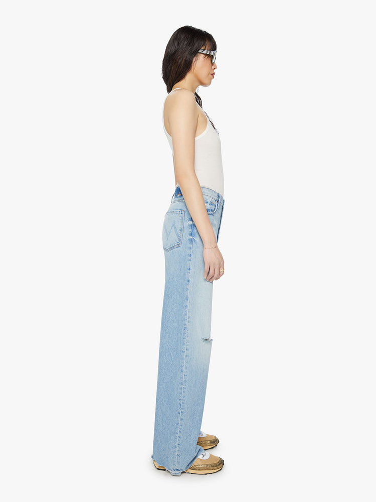 Side view of a woman super high-rise jeans with a loose wide leg, zip fly and a long 32-inch inseam with a chewed back hem in a light blue wash.