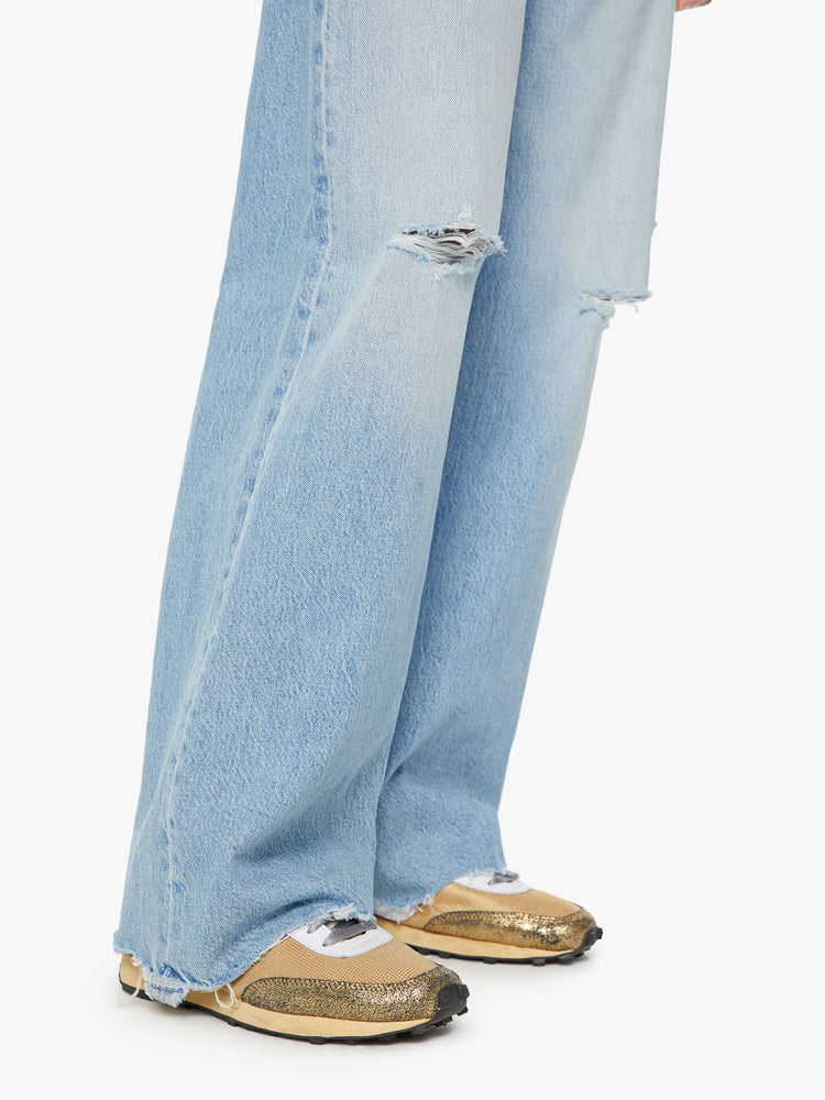 Hem close up view of a woman super high-rise jeans with a loose wide leg, zip fly and a long 32-inch inseam with a chewed back hem in a light blue wash.