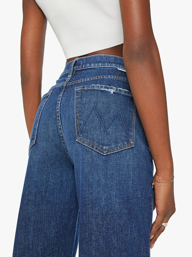 Close up view of a woman super high-waisted jeans with a straight barrel leg and a cropped inseam with a clean hem in a dark blue wash.