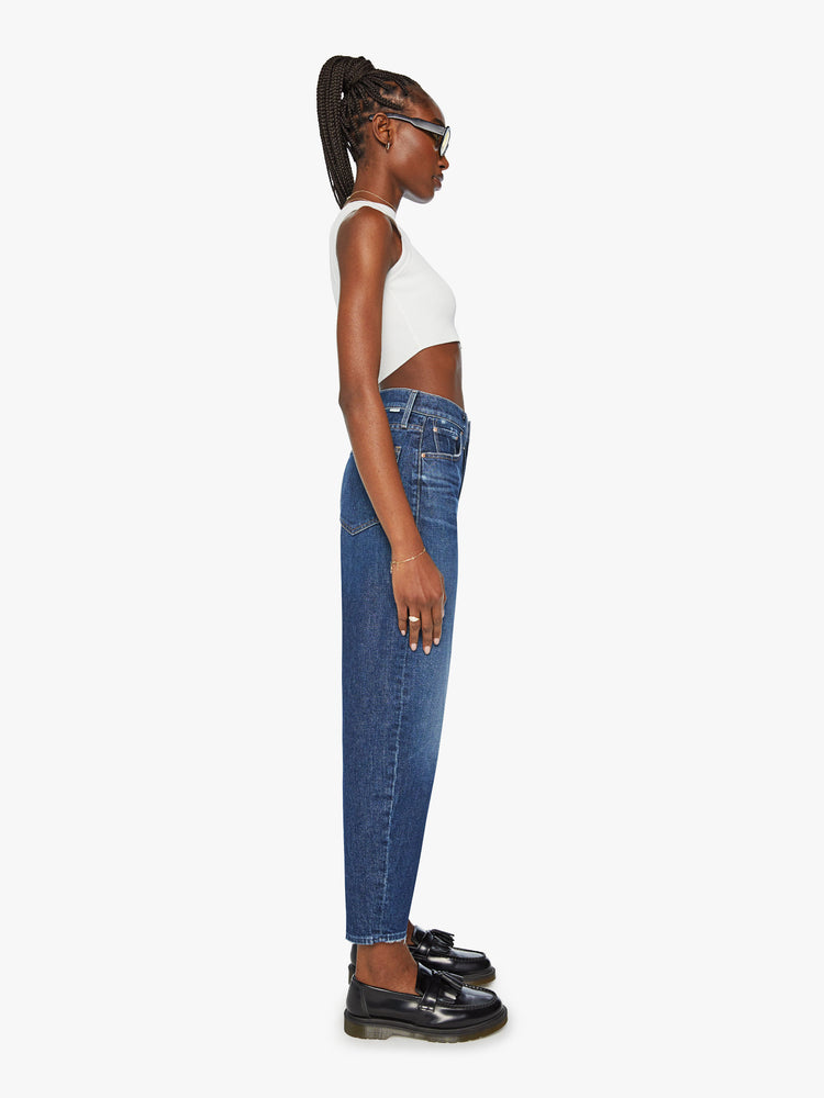 Side view of a woman super high-waisted jeans with a straight barrel leg and a cropped inseam with a clean hem in a dark blue wash.