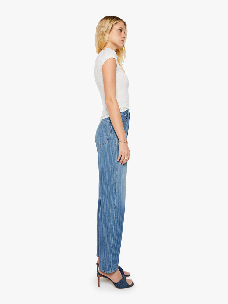Side view of a woman in a mid-blue with Japanese pinstripes in white and fading at the knees wide-leg pant with a zip fly, high rise and a 32-inch inseam with a clean hem.