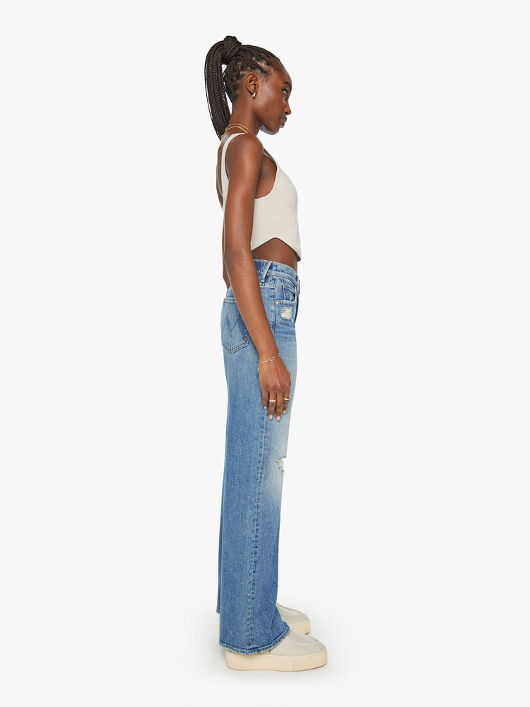 Side view of a woman super wide-leg jeans with a high rise and a long 32-inch inseam with a chewed hem in a mid-blue wash.