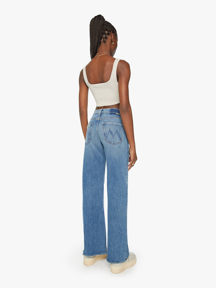 Back view of a woman super wide-leg jeans with a high rise and a long 32-inch inseam with a chewed hem in a mid-blue wash.
