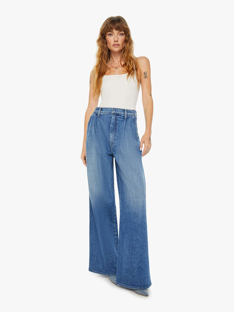 Front view of a woman medium blue super high-rise, wide-leg jeans are designed with a pleated waistband, slightly dropped crotch, side slit pockets and a long inseam.