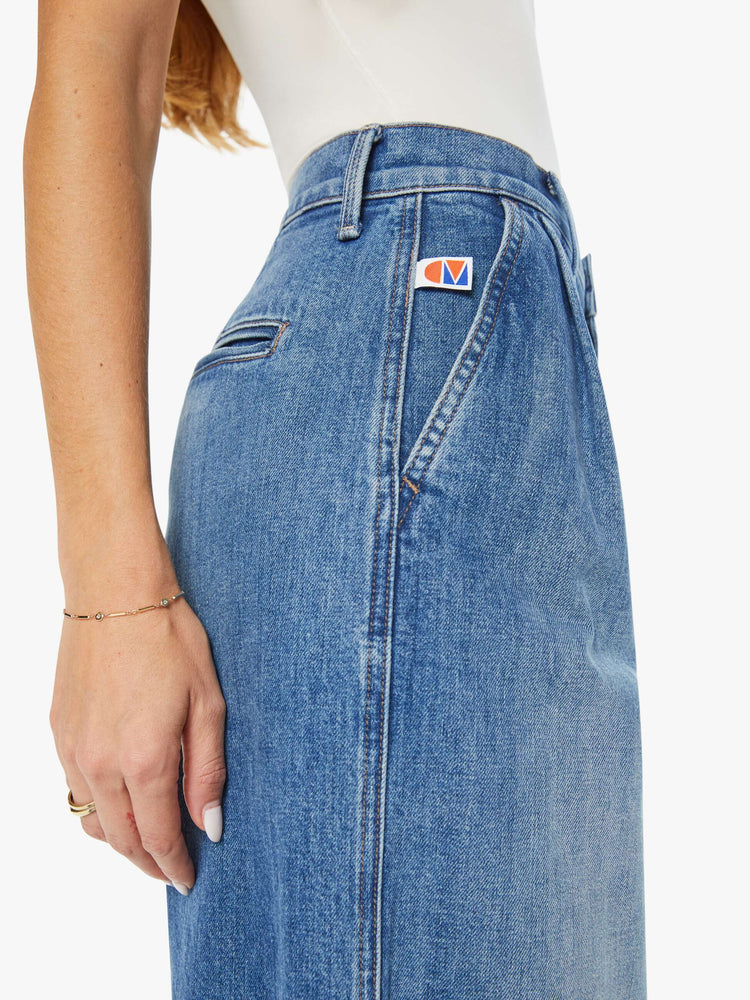 Close waist view of a woman medium blue super high-rise, wide-leg jeans are designed with a pleated waistband, slightly dropped crotch, side slit pockets and a long inseam.