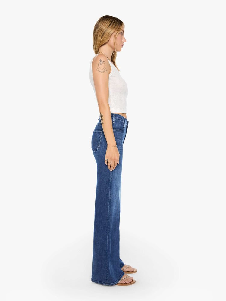 Side view of a woman wearing dark blue high rise jeans featuring a long inseam and wide leg.