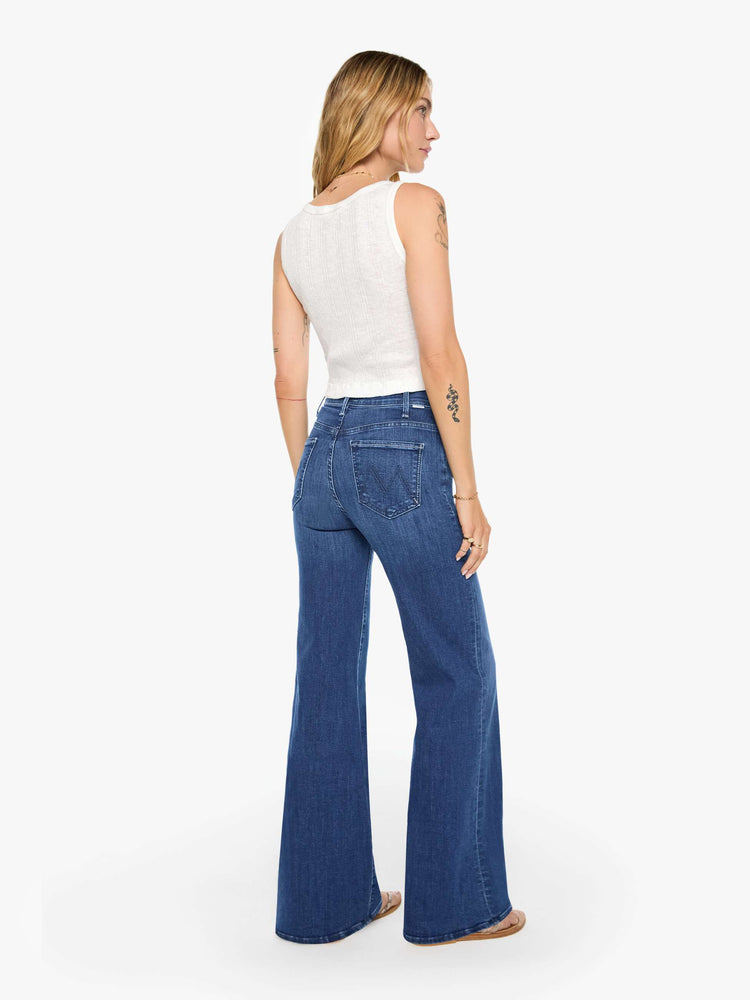 Back view of a woman wearing dark blue high rise jeans featuring a long inseam and wide leg.