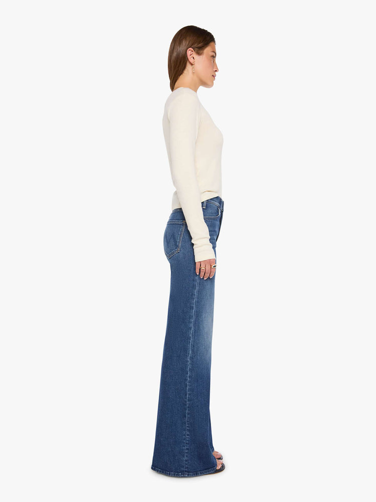 Side view of a woman in a mid blue wide leg jeans with a high rise, 33 7/8 inch inseam and a clean hem. 