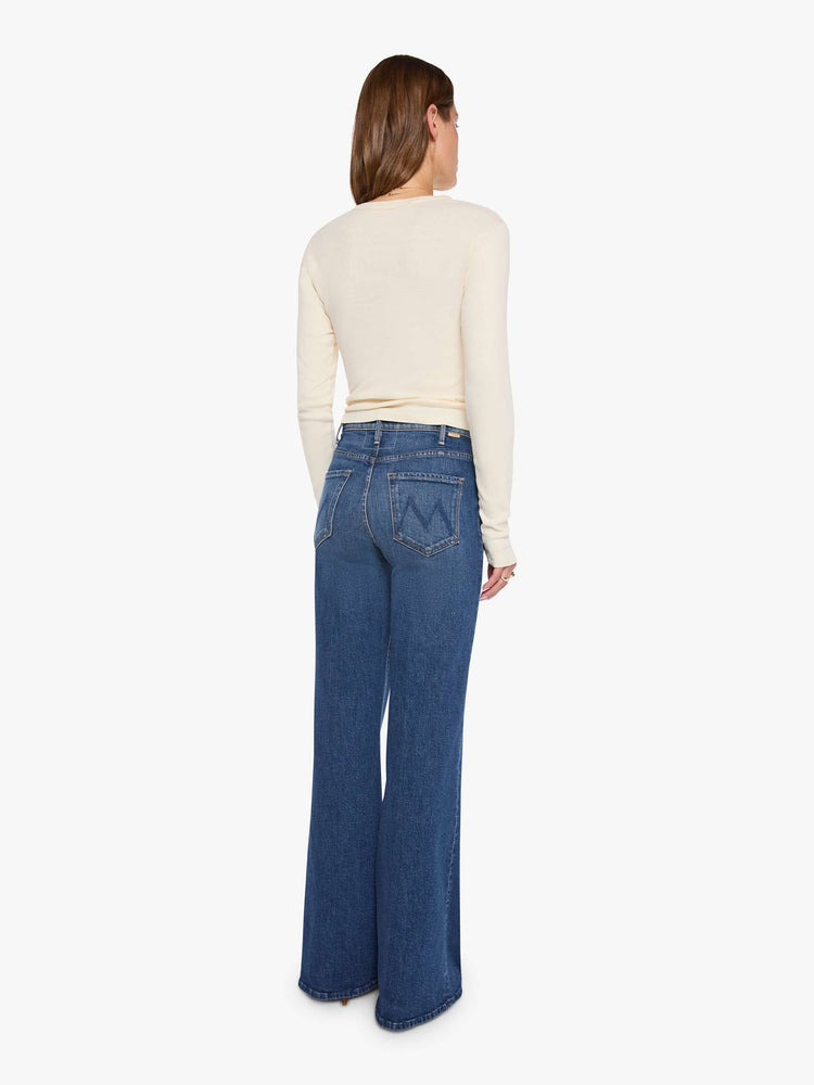 Back view of a woman in a mid blue wide leg jeans with a high rise, 33 7/8 inch inseam and a clean hem. 