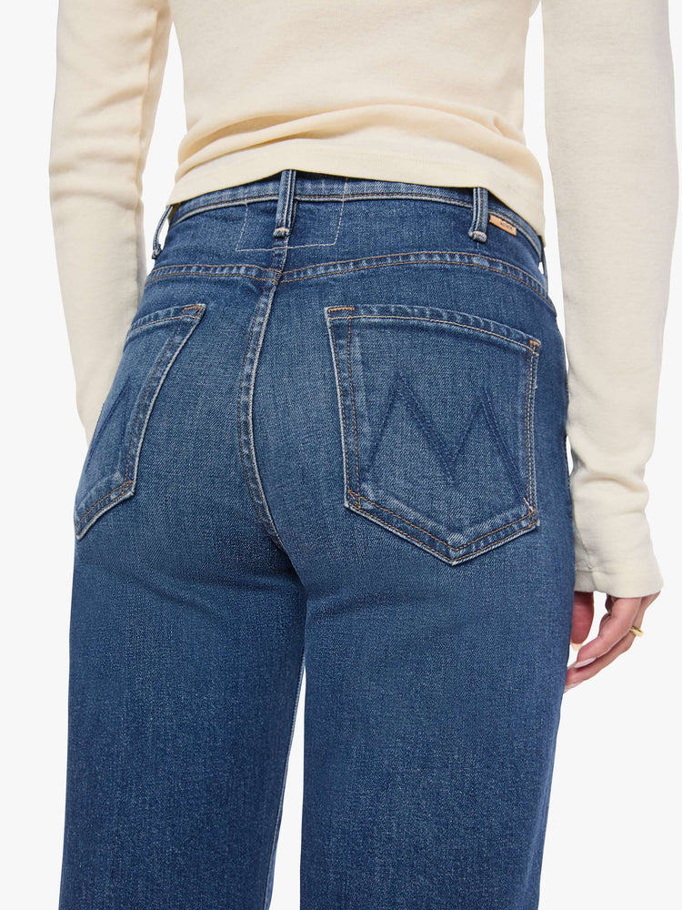 Close up view of a woman in a mid blue wide leg jeans with a high rise, 33 7/8 inch inseam and a clean hem. 