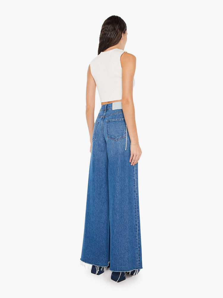 Back  view of a woman mid blue wash high-rise with a flowy wide-leg, slit pockets, seams down the front, a 32-inch inseam and a frayed hem.