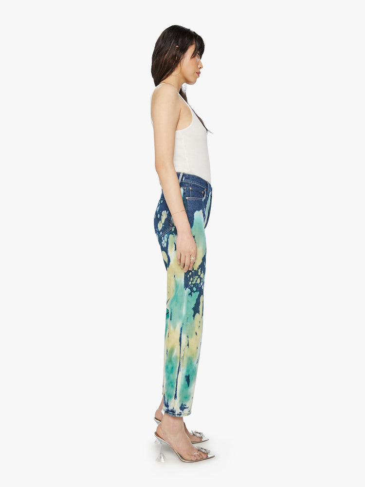 Side view of a woman high rise, straight leg with a clean hem in a dark blue wash with bleached and tie-dyed details in seafoam green and yellow.