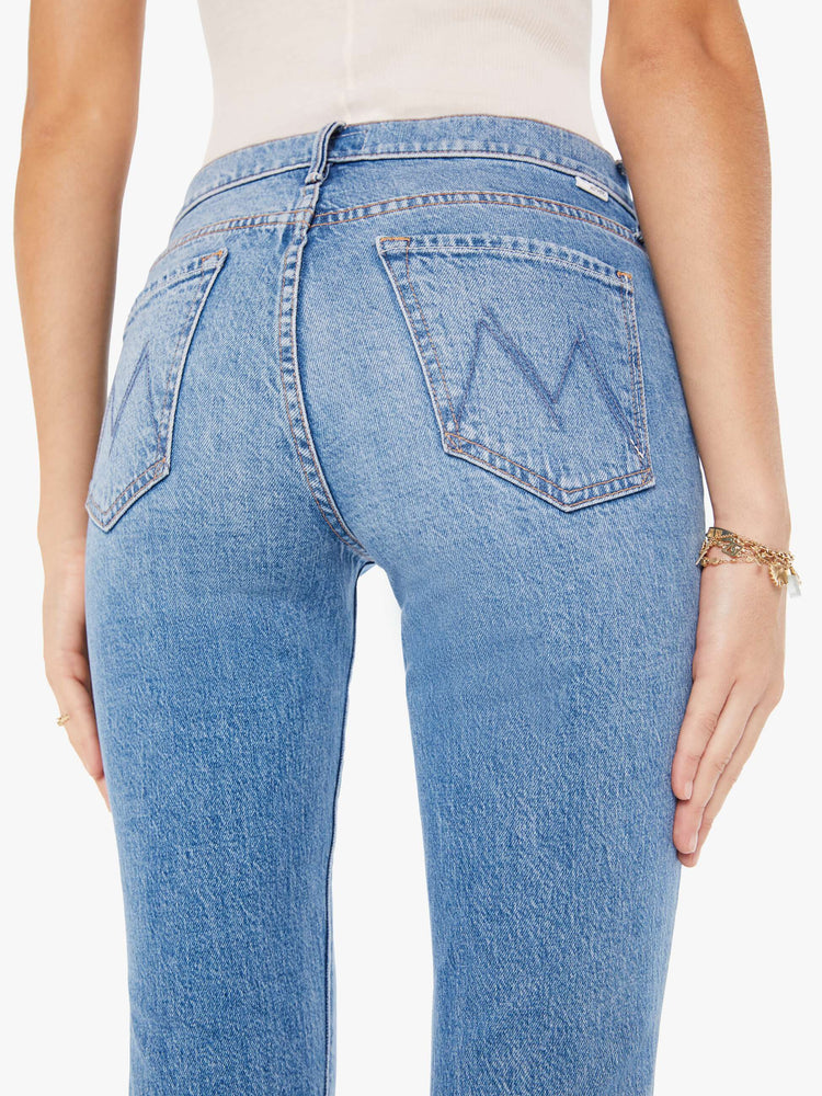 A close up back view of a woman wearing a medium blue wash jean featuring a mid rise.