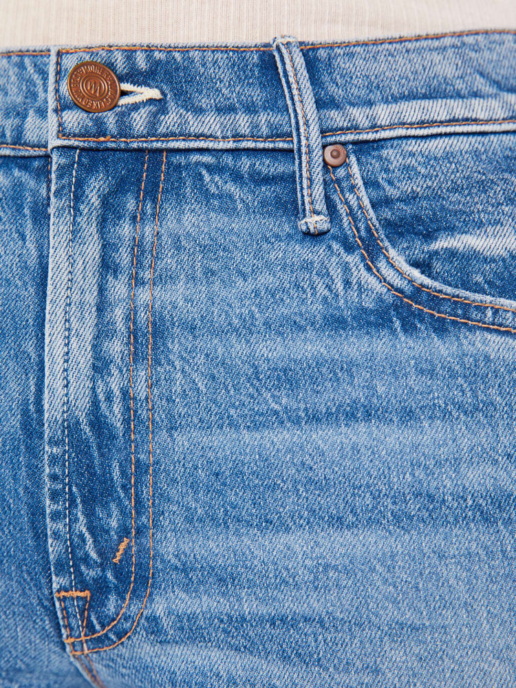 A close up swatch detail view of a medium blue wash jean featuring copper hardware and contrast brown thread,