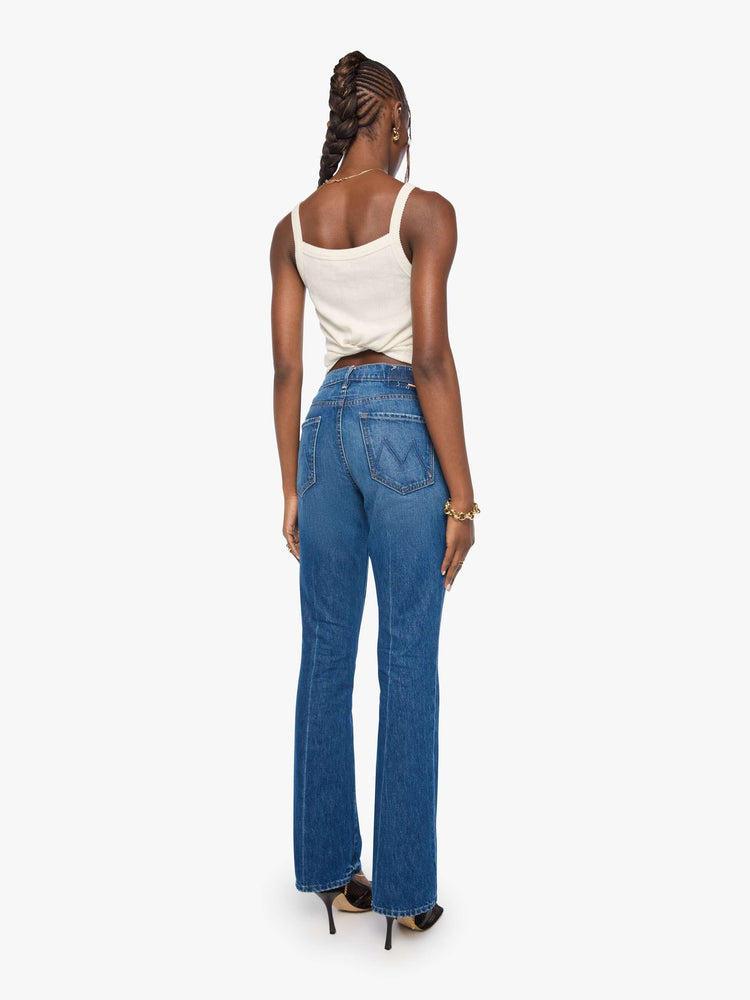 Back view of a woman in blue bootcut jeans with a mid rise, zip fly and a long 32-inch inseam with a clean hem.
