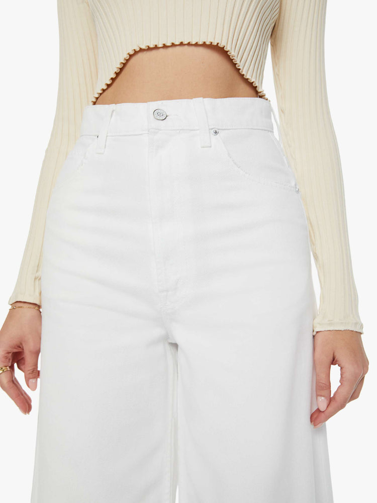 Detailed front view of a woman in slouchy off-white jeans that have a super-high rise and feature a loose, full leg with a pretzel-detailed button.
